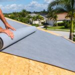 Roofer installing synthetic underlayment on a residential roof deck in a Florida neighborhood with palm trees
