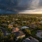 Aerial view of a Florida suburban neighborhood with tile and shingle roofs under dramatic storm clouds approaching Tampa Bay